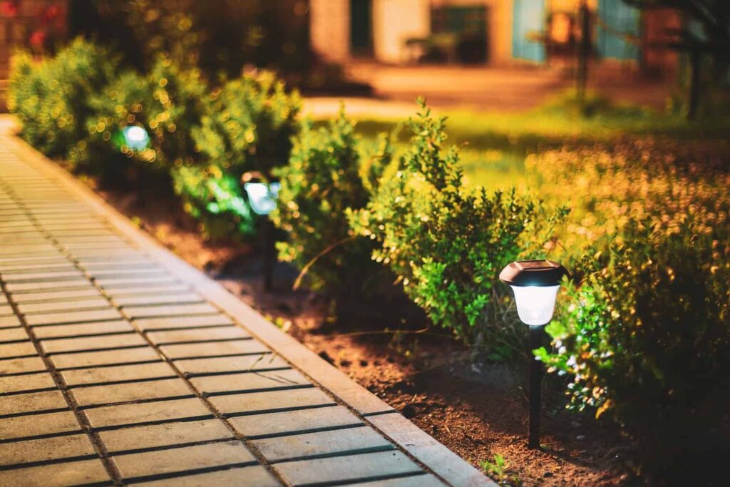 Vista notturna di un'aiuola illuminata da lanterne a risparmio energetico alimentate a energia solare lungo la strada principale del cortile che porta alla casa